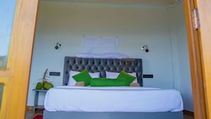 A bedroom with a wooden ceiling, a bed with a tufted headboard, and a nightstand with a plant. - Tunnel Top Inn Ella (Ella)