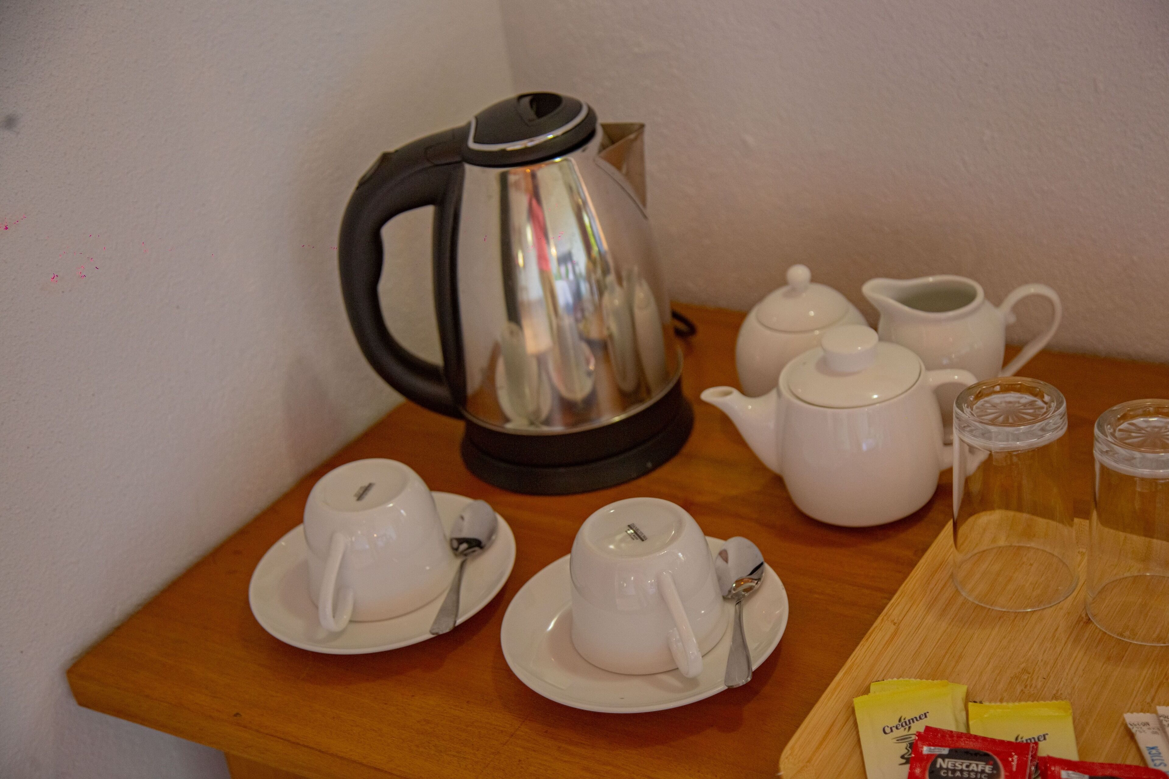 Ein Tisch mit Wasserkocher, Teekanne, Tassen, Untertassen und Sahnepäckchen.