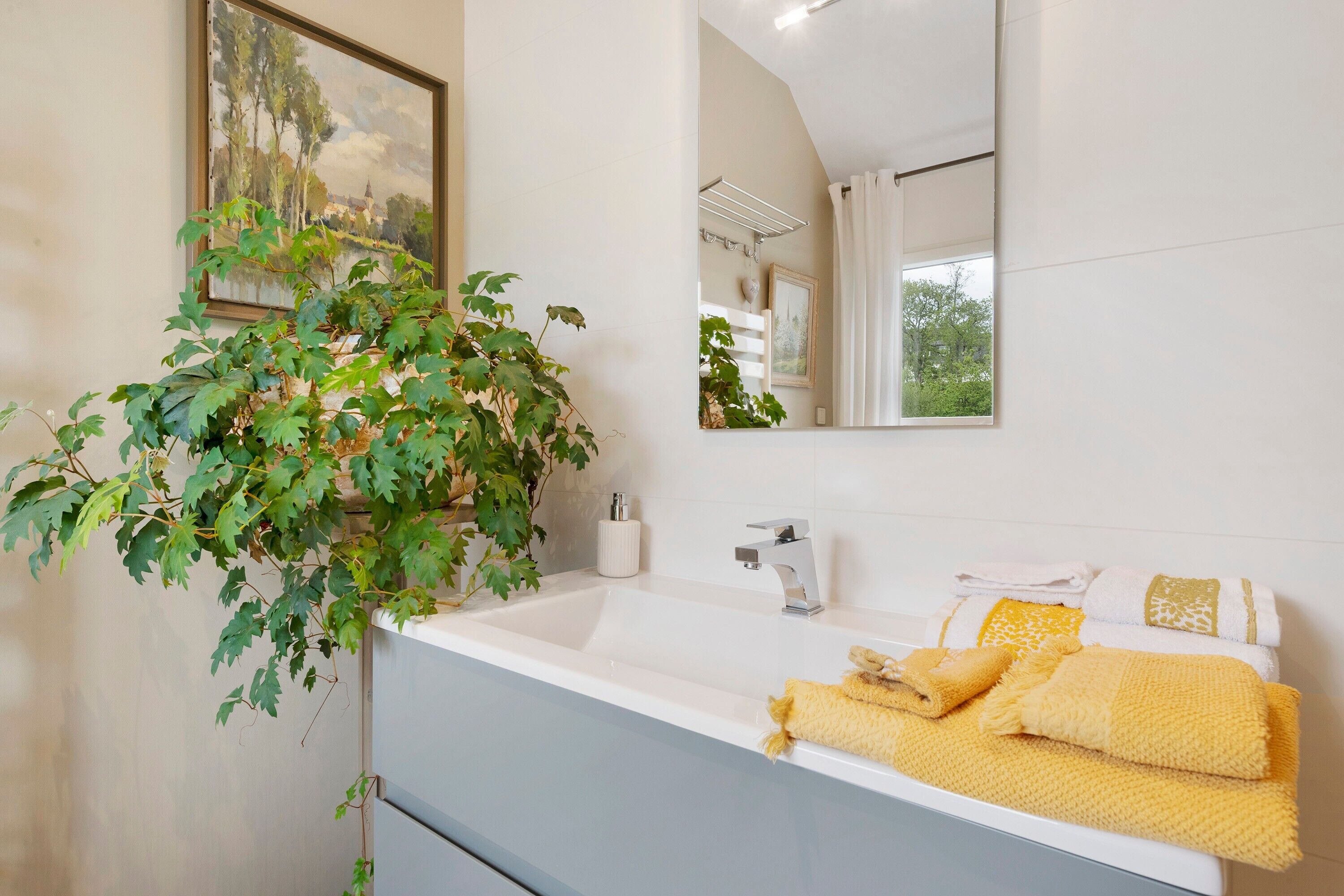 Une salle de bain avec un lavabo blanc, un miroir, une plante suspendue et des serviettes.