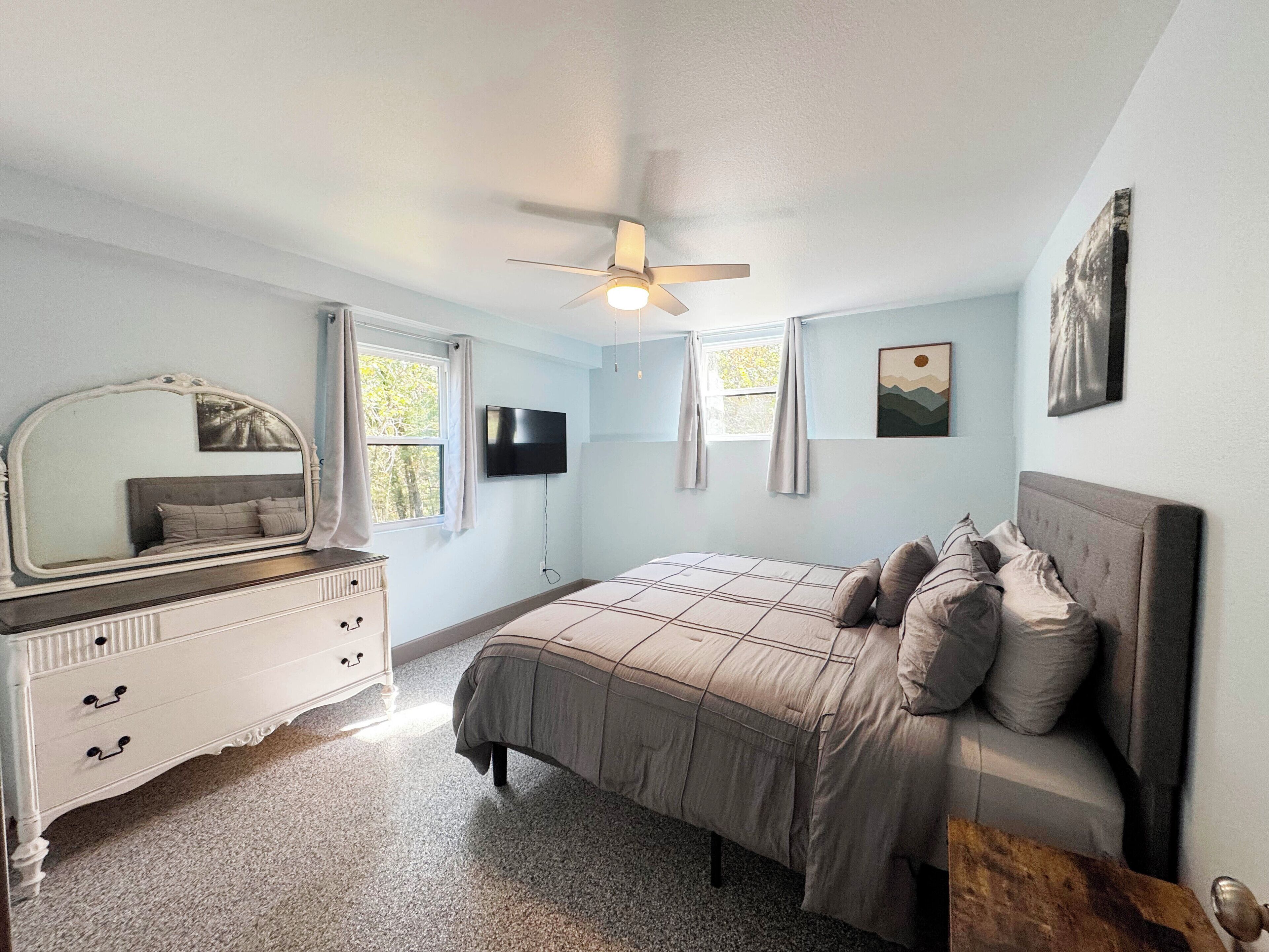 Ein Schlafzimmer mit Bett, Kommode, Deckenventilator, Fernseher und Kunstwerken.