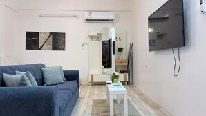 A modern living room with a blue sofa, a white side table, a flat-screen TV mounted on the wall, and a mirror above a wooden cabinet. - Maskn Al Bader (Madinah)
