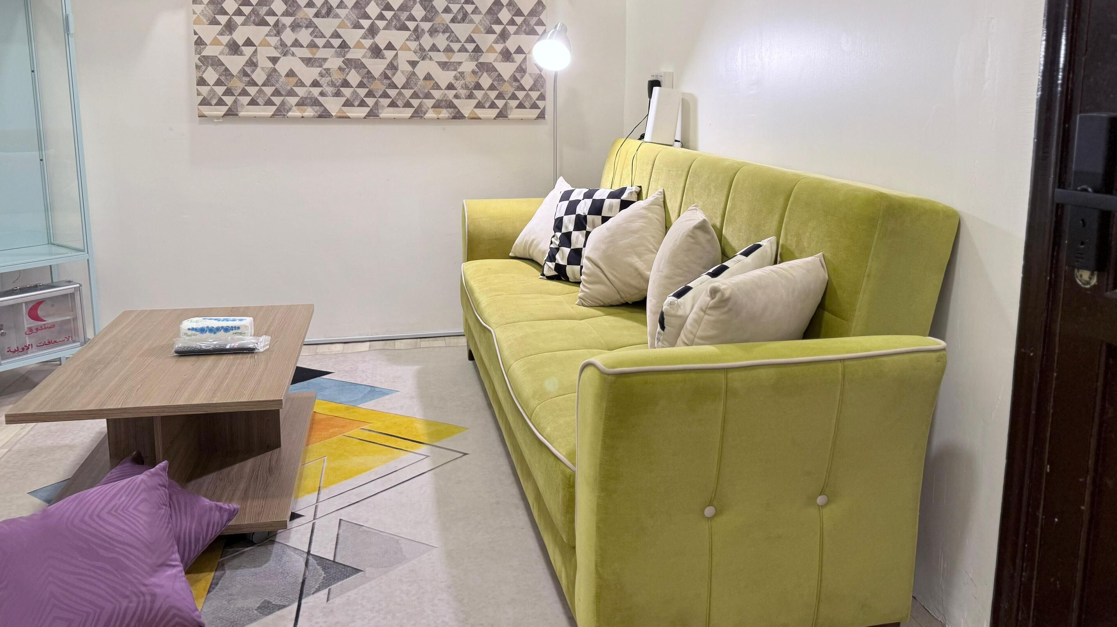 A room with a green sofa, a wooden coffee table, and a patterned rug.