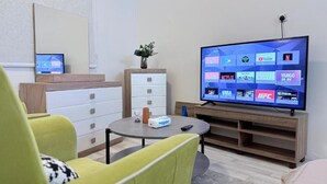 A modern living room with a flat-screen TV displaying various streaming services, a small table with a remote control, and a decorative vase. - Maskn Al Bader (Madinah)