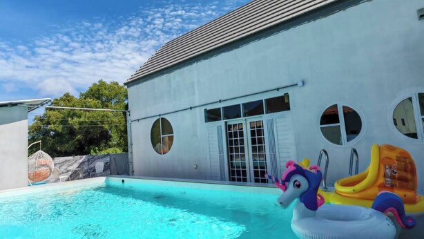 A swimming pool with a clear blue water surface, a white building with circular windows, and inflatable toys on the poolside. - Fantastic 3-bedroom with AC in charming in Pattaya Chon Buri (Chon Buri)
