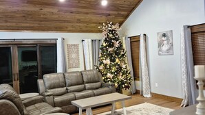 A cozy living room with a wooden ceiling, a large Christmas tree, a grey sofa, and a coffee table. - Murphy House at Pickwick (Tishomingo County)