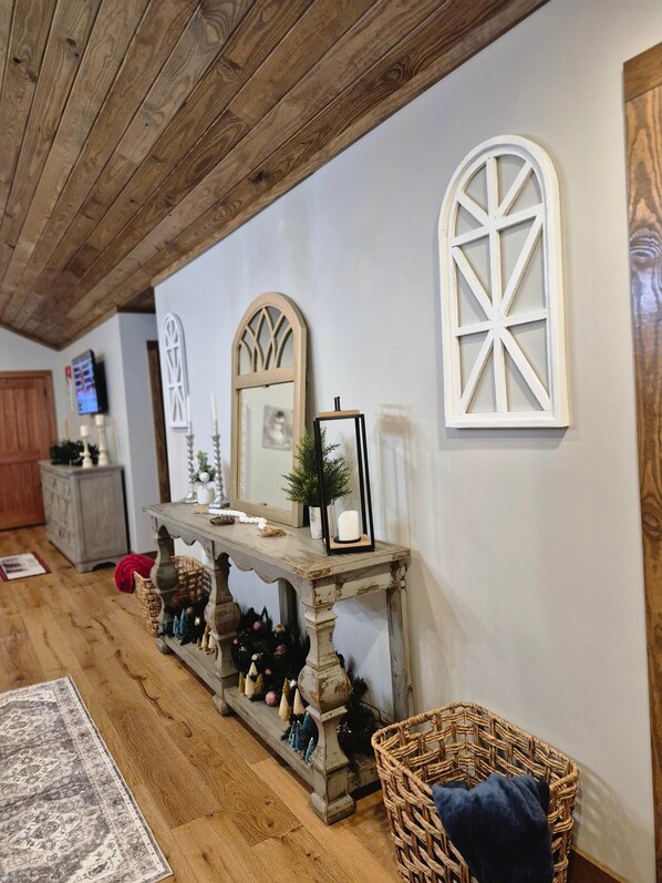 A room with a wooden ceiling, a console table with decorative items, a mirror, and a window with a white frame.