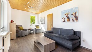 Un salon moderne avec un plafond en bois, un canapé gris, une table basse en bois et un tableau représentant des vaches accroché au mur.