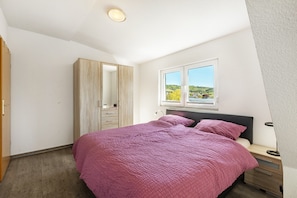 Ein Schlafzimmer mit Bett, Schrank, Nachttisch, Lampe und einem Fenster mit Aussicht.