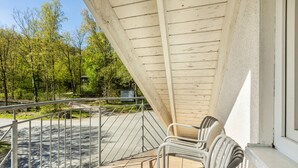 Un balcon avec des balustrades en métal, un plafond en bois et une vue sur une zone boisée.