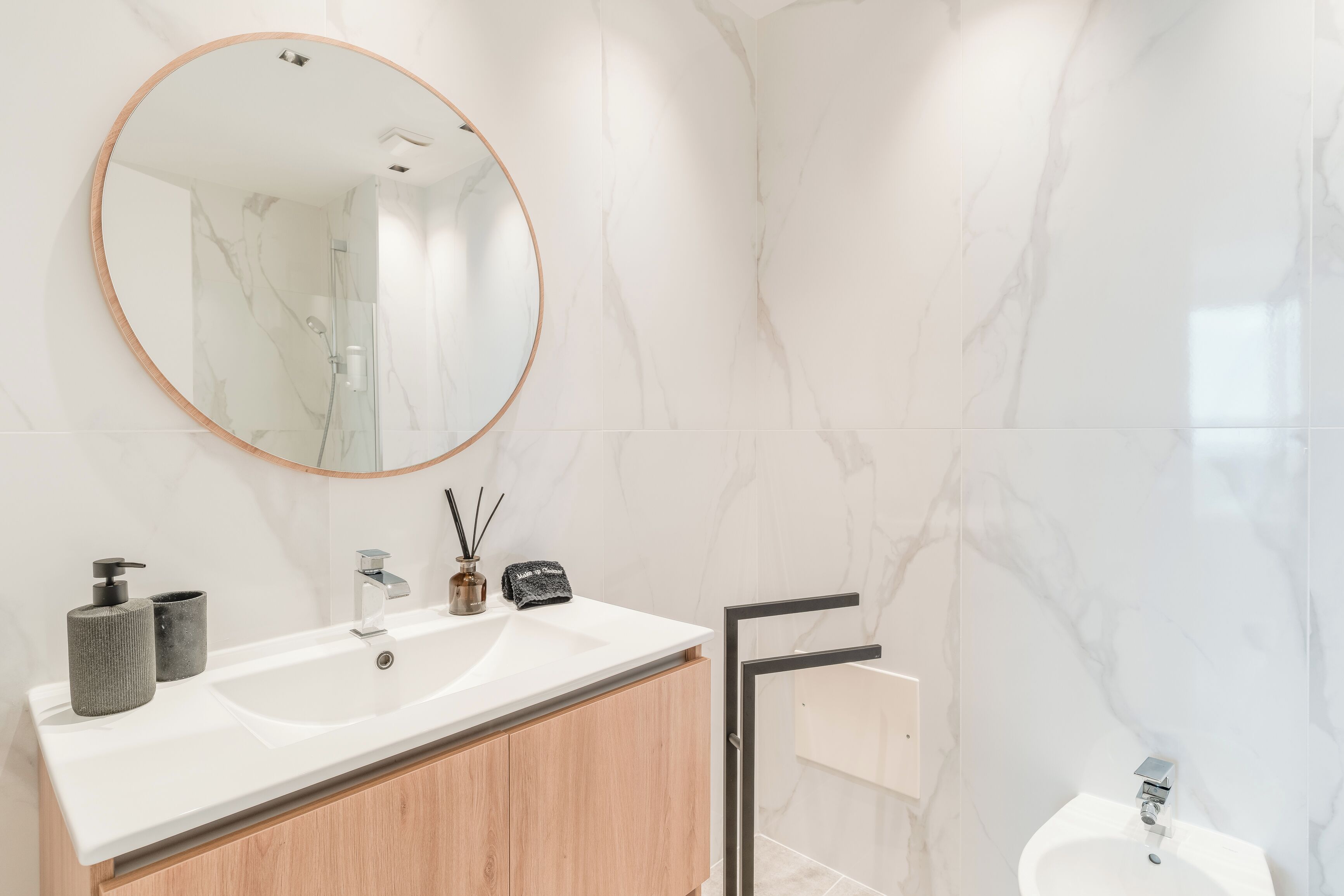 A bathroom with a round mirror, two sinks, a shower, and marble walls.