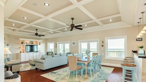 A spacious living room with a dining area, wooden floors, ceiling fans, and large windows. - Bright Beachfront Retreat, Elevator, Dog Friendly, Quick Beach Access (Galveston)