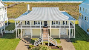 A large, two-story house with a central staircase, a covered porch, and a view of the ocean. - Bright Beachfront Retreat, Elevator, Dog Friendly, Quick Beach Access (Galveston)