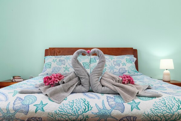 A bed with a blue and white floral bedspread, two towels arranged in a heart shape, and pink flowers on the bed. - Casa de Reyes (Noord)
