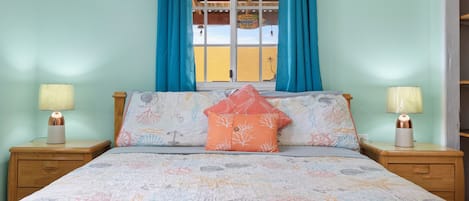 A bedroom with a bed, two bedside tables with lamps, a window with curtains, and a view of the outside.
