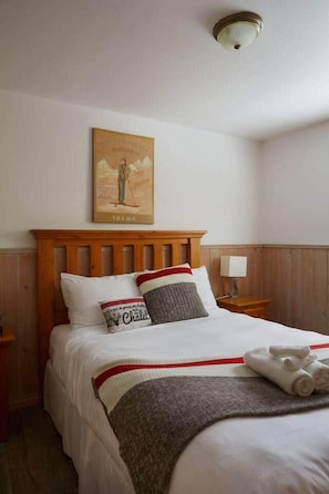Un lit bien fait, avec une tête de lit en bois, un tableau accroché au mur et une table de chevet sur laquelle se trouve une lampe.