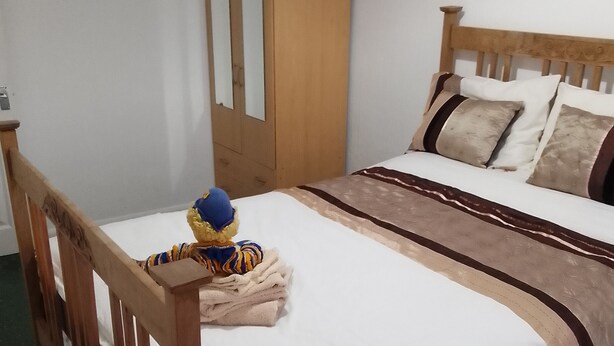 Ein ordentlich bezogenes Bett mit Holz Kopfteil, einem Holzschrank und einem Plüschtier auf dem Bett.