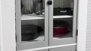 Ein weißer Schrank mit Glastüren, der Küchengeräte und Kochutensilien beherbergt.