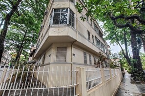 Ein mehrstöckiges Gebäude mit einer Hausecke, einer Einfahrt mit Tor und Bäumen rund um das Anwesen.