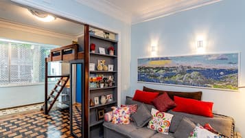 Una sala de estar con un sofá gris, almohadas coloridas, una escalera de madera y una estantería.