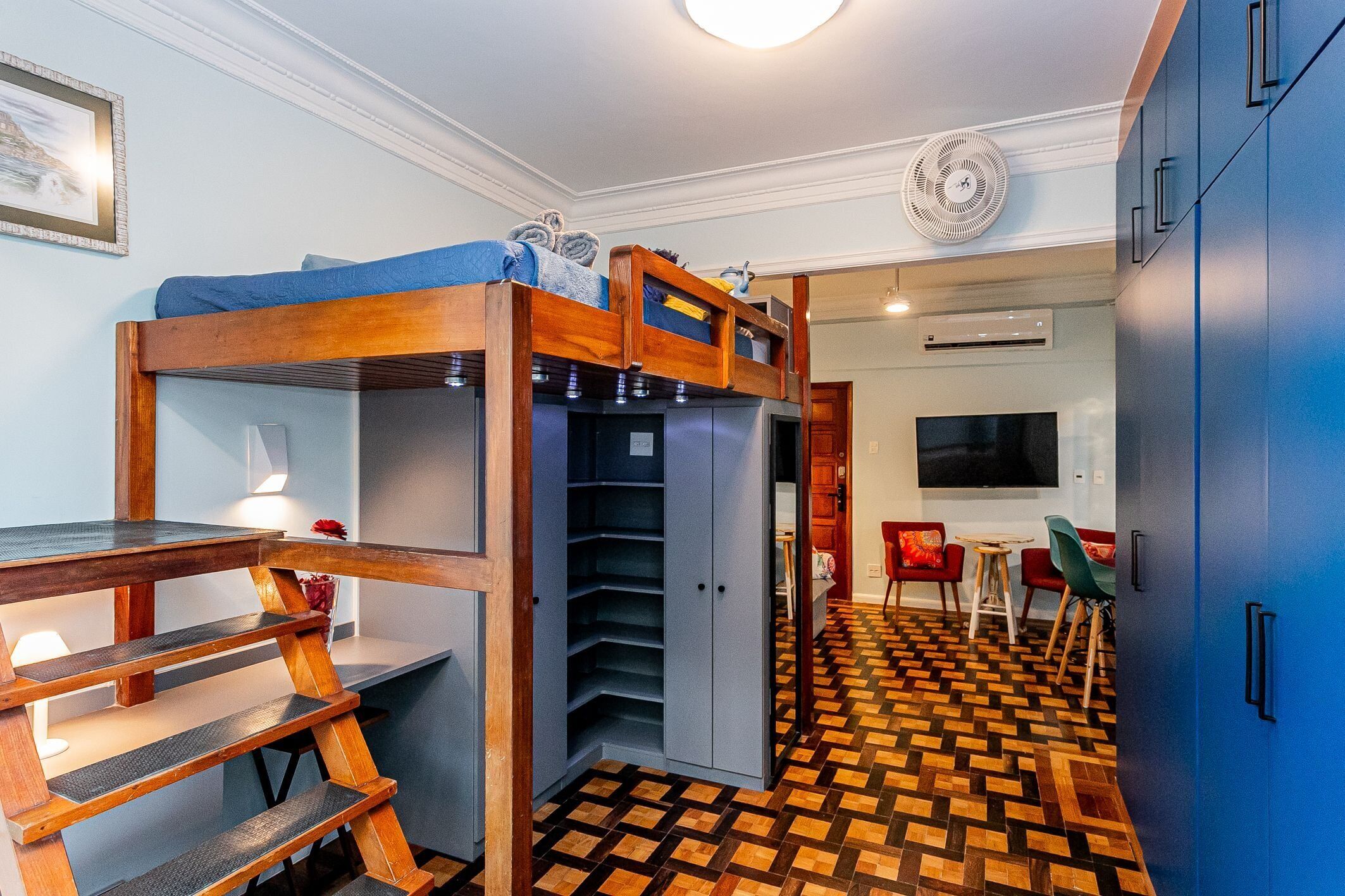Een kleine kamer met een stapelbed, een bureau met lamp, een tafeltje, een stoel en een televisie.
