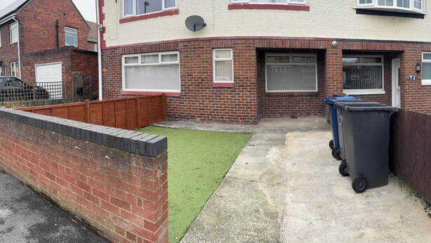 A residential property with a brick facade, a small front yard with artificial grass, and two wheelie bins. - Ground Floor Property - Sleeps 2 - Parking - Garden (Jarrow)