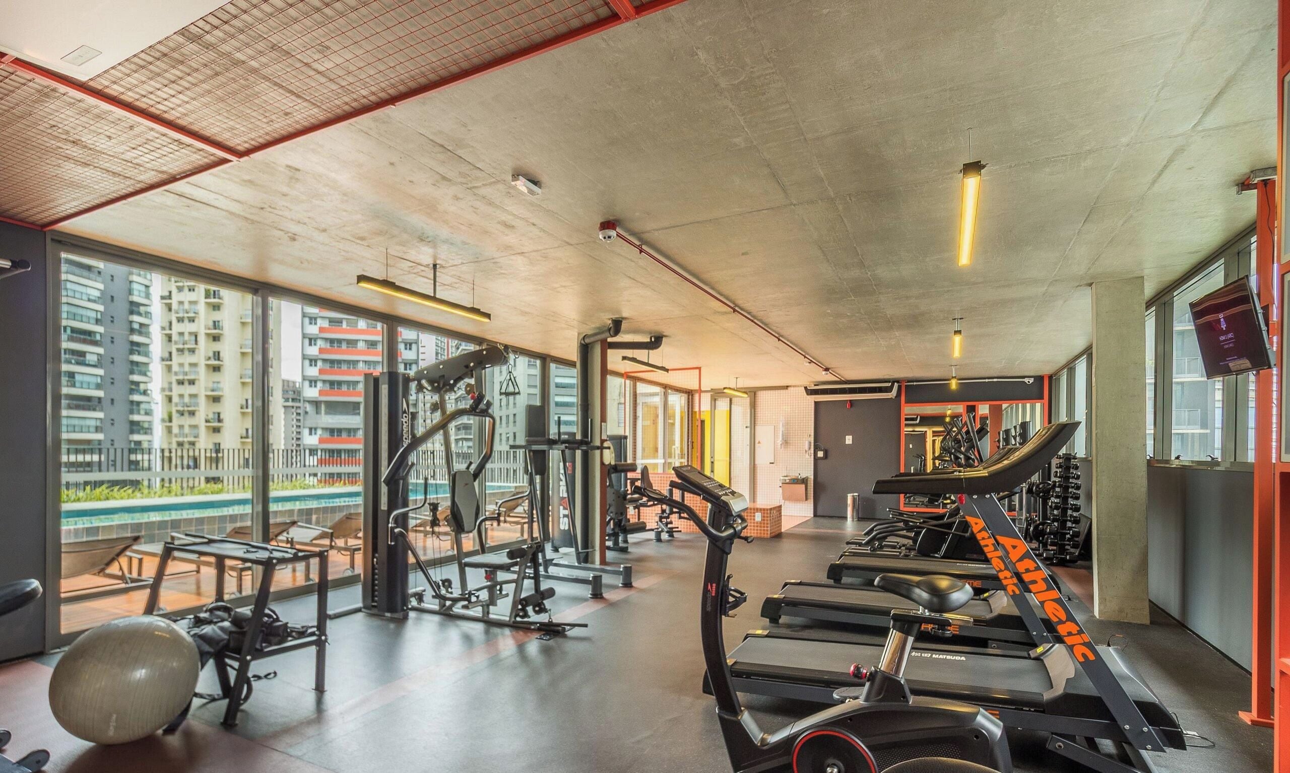 A gym with various exercise equipment, large windows, and a view of high-rise buildings.