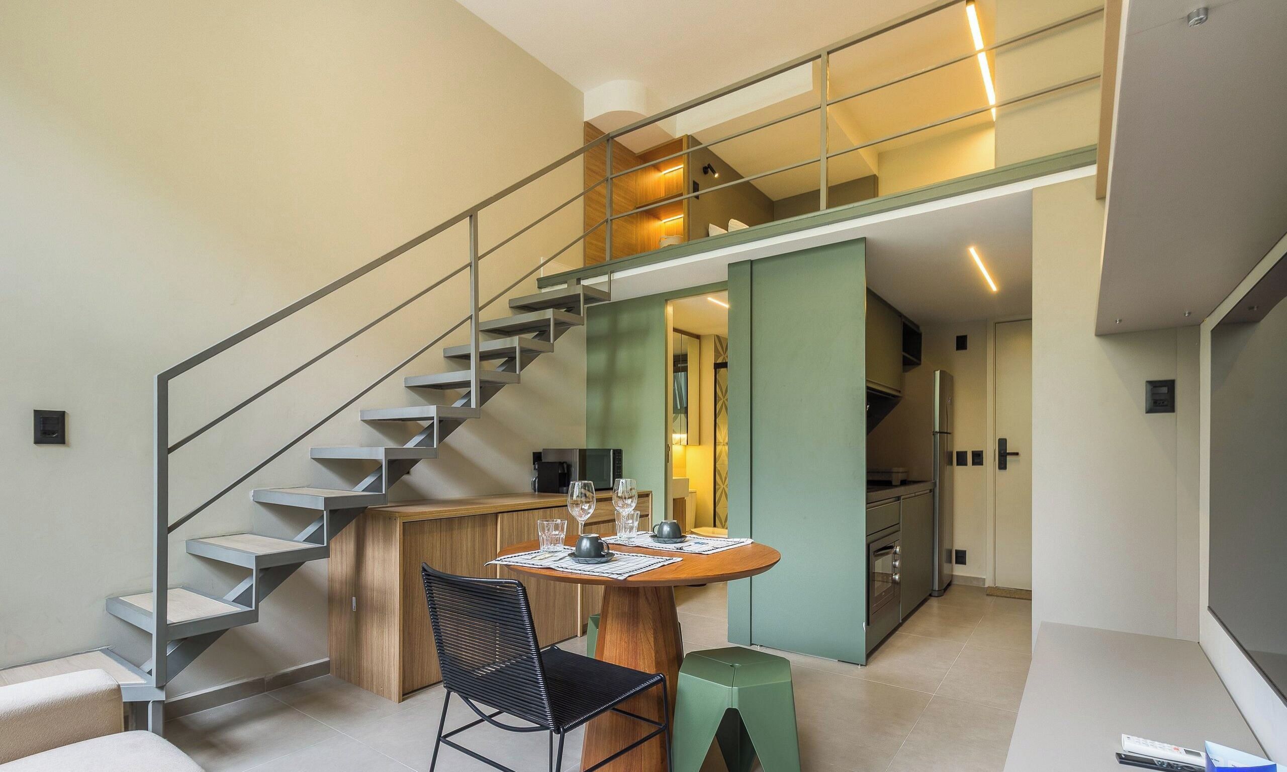Ein modernes Interieur mit einer Treppe, einem Essbereich mit Tisch für zwei Personen und einer Küche im Hintergrund.