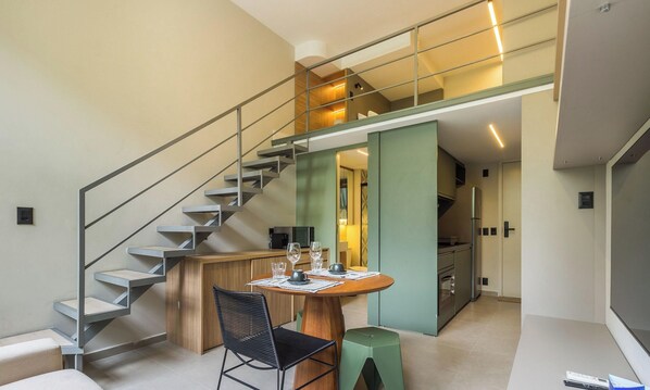 A modern interior with a staircase, a dining area with a table set for two, and a kitchen in the background. - Modern Accommodations in a Building With a Pool in the Heart of SP - Yhes (São Paulo)
