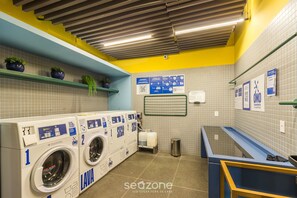 A laundromat with two washing machines, a trash bin, and a blue counter. - Modern Accommodations in a Building With a Pool in the Heart of SP - Yhes (São Paulo)