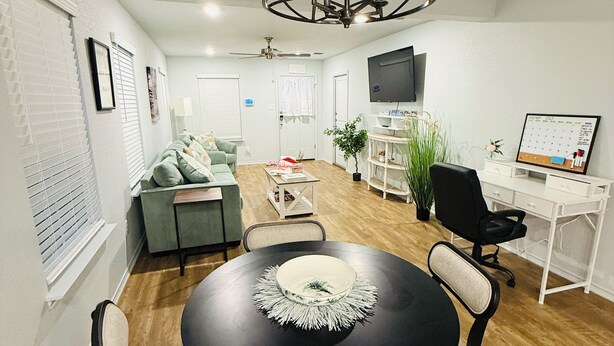 A modern living room with a dining area, a TV mounted on the wall, and a ceiling fan.