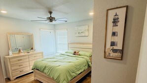 A bedroom with a bed, dresser, ceiling fan, and artwork on the wall.