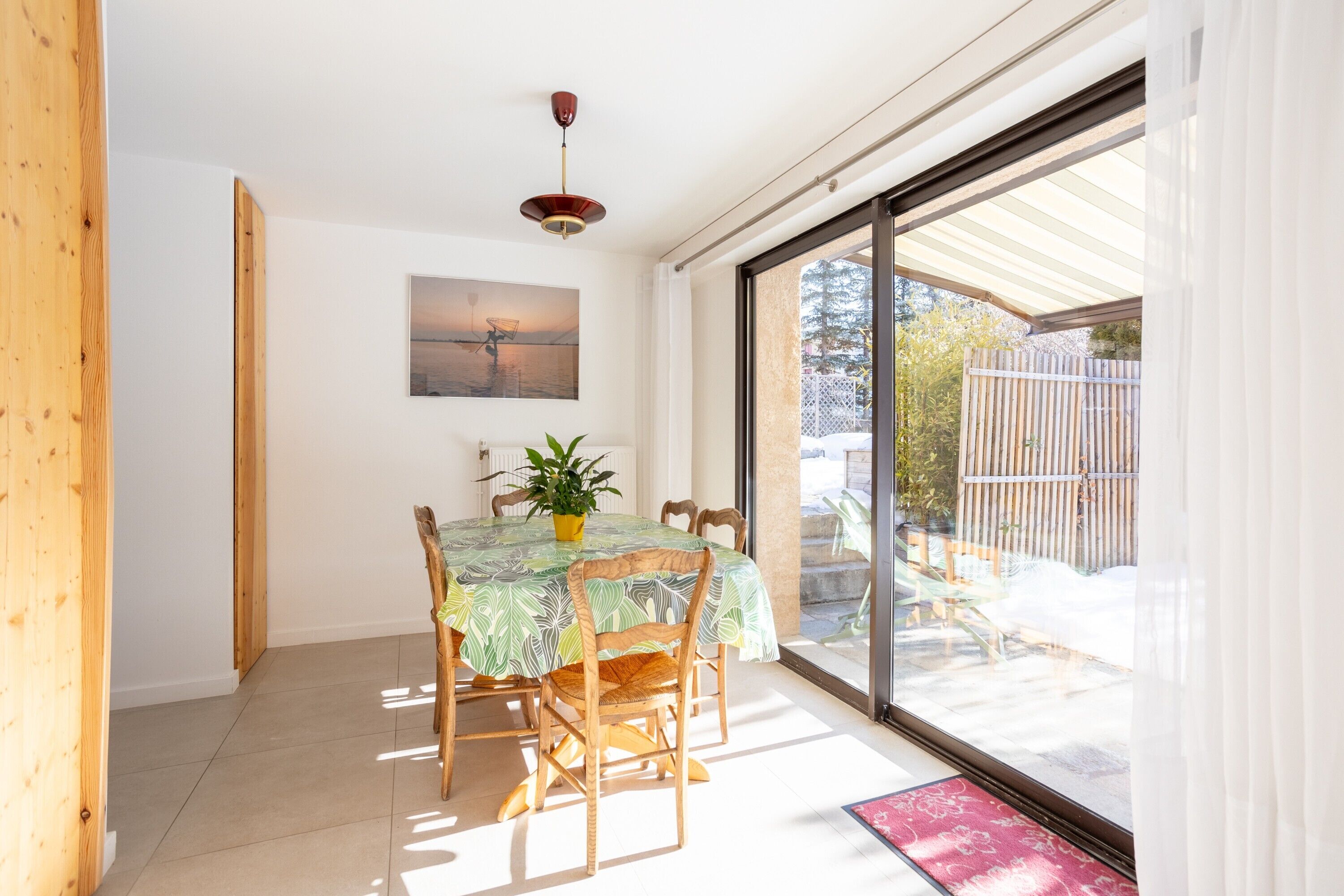 A dining area with a table and chairs, a potted plant, and a painting on the wall.