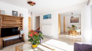 A living room with a wooden entertainment unit, a glass coffee table, and a purple sofa. - Au fil du Réguinier – Seasonal Rental Cottage (Briançon)