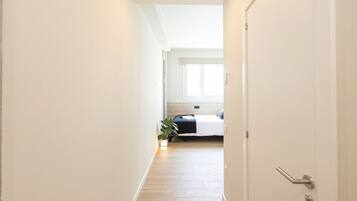 A narrow hallway with a bed at the end, a plant, and a door with a handle.