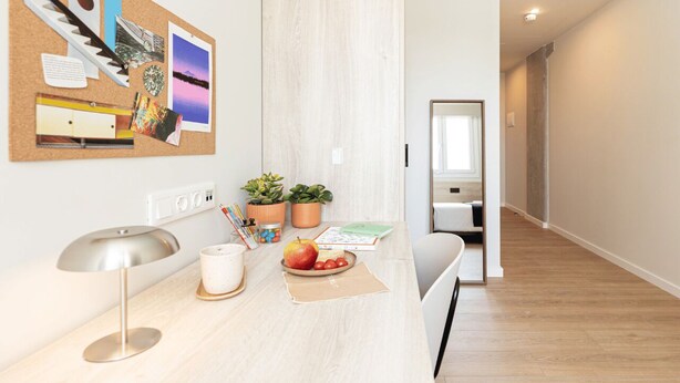 A modern kitchen with a light wood countertop, a corkboard with photos and notes, and a view into the dining area. - Yugo Terrassa (Terrassa)