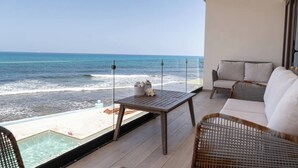 A balcony with a wooden table, wicker chairs, and a view of the ocean. - Wake up to turquoise waters at Isla Bliss 🌴 — a luxury 3-bedroom oceanfront condo just minutes from Isla Mujeres’ best dining and beaches. Enjoy a 90" Smart TV, stunning views, fast WiFi, and easy self-check-in for the perfect island escape. 🌊✨ (Isla Mujeres)