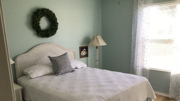 A neatly made bed with a white quilt, a decorative pillow, and a wall-mounted wreath. - Live the Villages lifestyle in  this 2 bedroom beauty (The Villages)