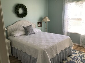 A neatly made bed with a white quilt, a decorative pillow, and a wall-mounted wreath.