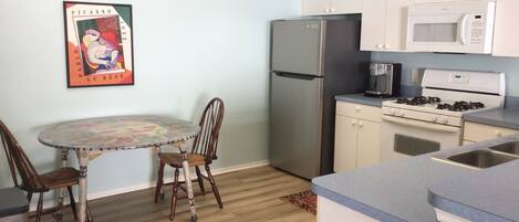 A compact kitchen with a refrigerator, microwave, stove, and a dining table with chairs.
