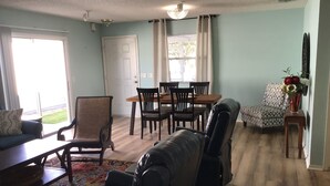 A living room with a sofa, a leather chair, a dining table with chairs, a patterned rug, and a vase with flowers on a side table. - Live the Villages lifestyle in  this 2 bedroom beauty (The Villages)
