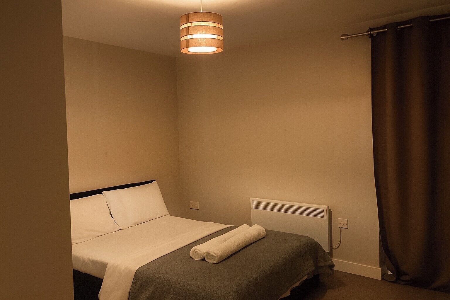 Une petite chambre avec un lit simple, un radiateur, un luminaire suspendu et un rideau.