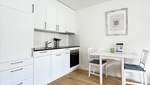 Ett modernt kök med vita skåp, en svart bänkskiva och en matplats med ett vitt bord och stolar.