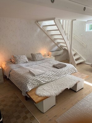 A bedroom with a large bed, a wooden bench, a white staircase, and a nightstand with a lamp. - Cozy holiday home with lots of light in quiet beautiful villa area. (lindome)