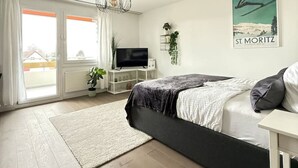 Une chambre à coucher avec un lit, une télévision, une plante et une affiche accrochée au mur.