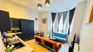 Eine moderne Küche mit dunklen Schränken, ein Essbereich mit einem blauen Sofa und ein großes Fenster mit Vorhängen.