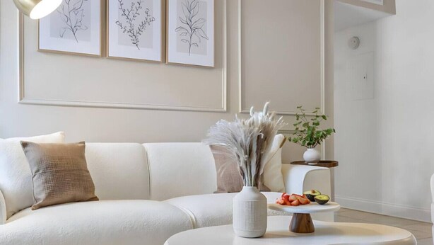 Un salon moderne avec un canapé blanc, une petite table d’appoint blanche et un vase contenant des plantes séchées.