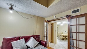 Quarto com sofá de couro vermelho, espalha cama cinza e porta de madeira com painéis de vidro.