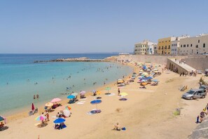 Ein Strand mit Menschen, Sonnenschirmen und Gebäuden im Hintergrund.