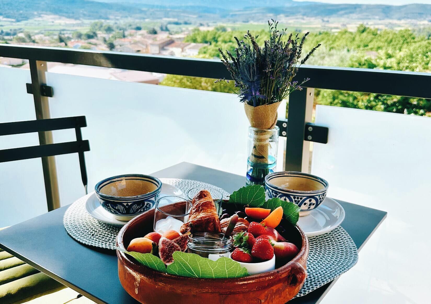 Ein Tisch mit Obstschale, zwei Kaffeetassen und Blumenstrauß auf einem Balkon mit Aussicht.