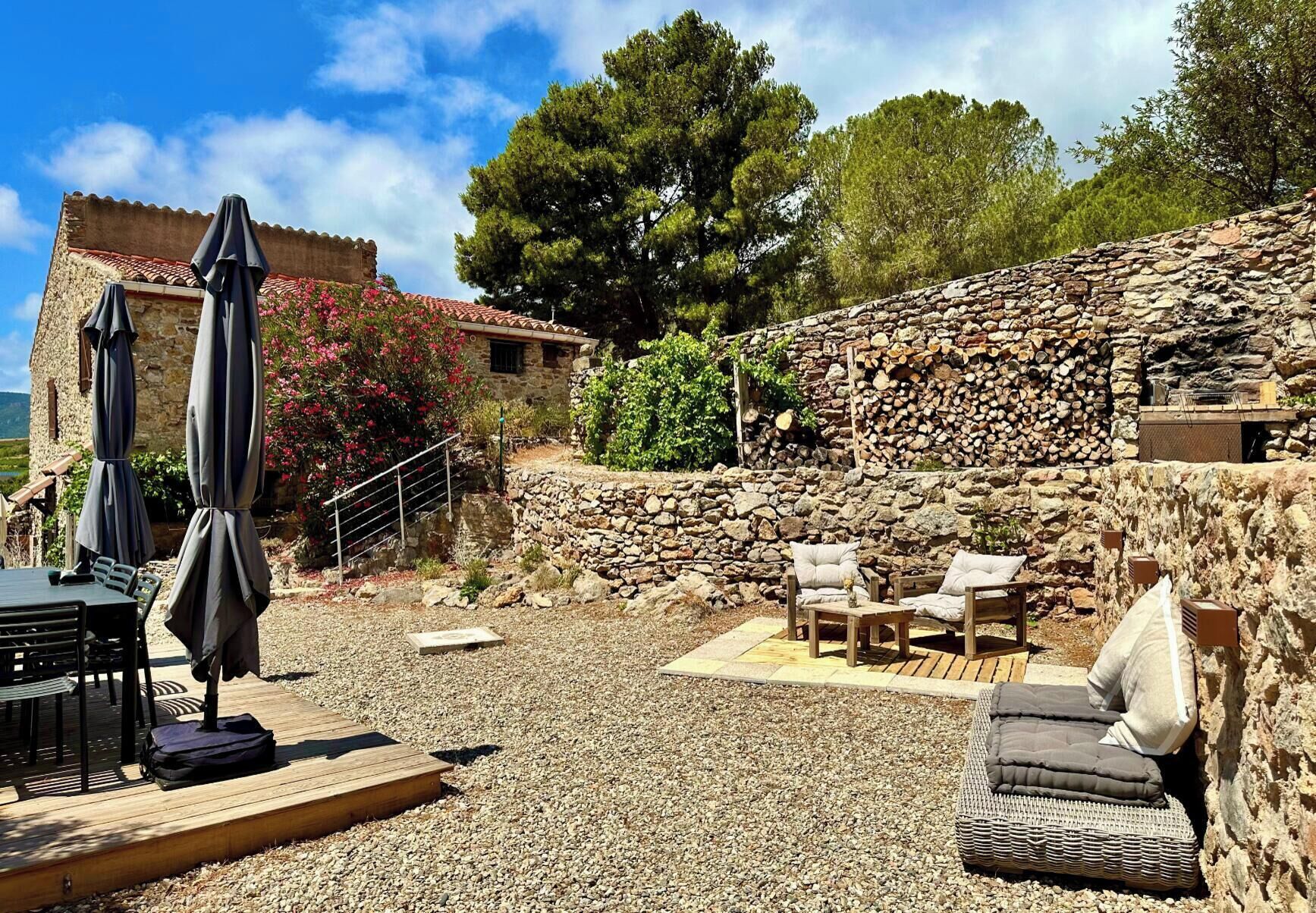 Uma área de pátio com paredes de pedra, móveis de exterior e uma mesa com guarda-sóis.